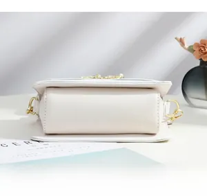 Détail de la base du sac à bandoulière blanc crème avec ses crochets dorés élégants
