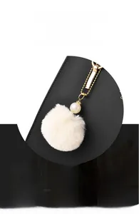 Dettaglio di un ciondolo in peluche bianco con catena dorata e perle su borsa in pelle nera