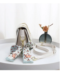 Detailed shot of an elegant cream PU leather crossbody bag with a decorative silk scarf accessory