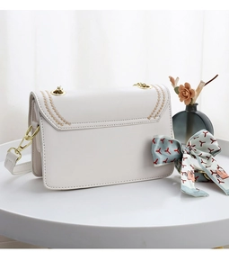 Detail of white leather shoulder bag with gold floral embroidery and decorative silk scarf