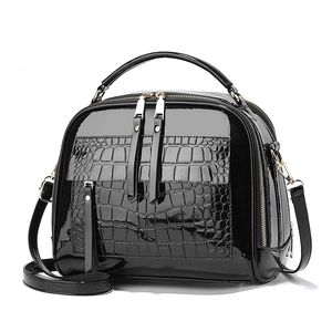 Sac à main noir brillant motif crocodile avec double zip et détails dorés sur fond blanc