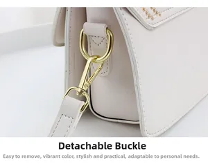 Detail of gold detachable metal buckle and fine embroidery on cream leather crossbody bag