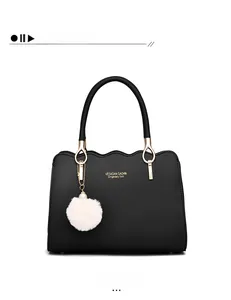 Dettaglio borsa nera in pelle con bordi a onde, logo dorato e ciondolo a pompon bianco
