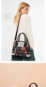 Detail of plaid handbag showing golden hardware charm and textured top handles