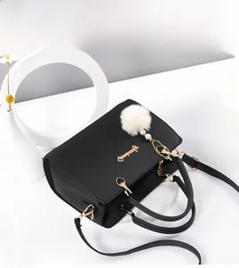 Dettaglio borsa nera in pelle con logo dorato e ciondolo con pompon bianco morbido
