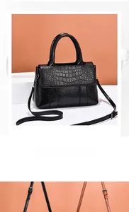 Detail view of black crocodile pattern flap and smooth leather strap on tote bag