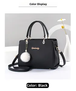 Dettaglio borsa a mano nera in pelle con logo dorato e ciondolo a pompon bianco