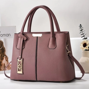 Detail view of lychee texture pink leather handbag with gold logo and metal charm