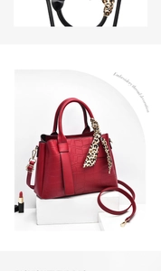 Macro detail of red crocodile texture handbag with silk scarf and gold ring handles