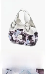 Detail of silver brand plate on white leather and floral fabric of a spacious tote bag