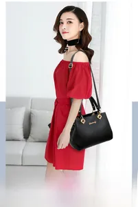 Detail of elegant black leather handbag with gold hardware held by woman in red dress
