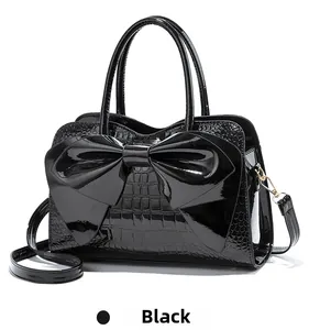 Detail of glossy black patent handbag with large bow and crocodile pattern texture