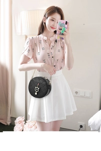 Detail of black round quilted crossbody bag with gold cat pendant on pink outfit