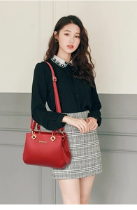 Detail of red leather handbag with gold logo and adjustable strap on a shoulder