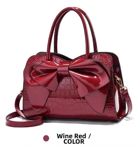Close-up of wine red glossy crocodile embossed leather handbag with large bow detail