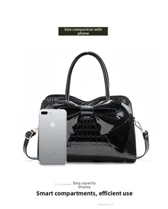 Detail shot of black crocodile-embossed patent leather bag size comparison with phone