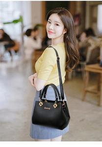 Detail of black pebbled leather handbag with gold hardware worn by a model in a cafe
