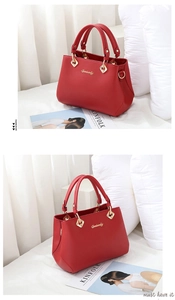 Detail of red leather handbag with gold logo and hardware on white bedding background