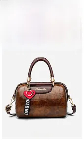 Detailed front view of brown crocodile pattern boston bag with heart charm and strap