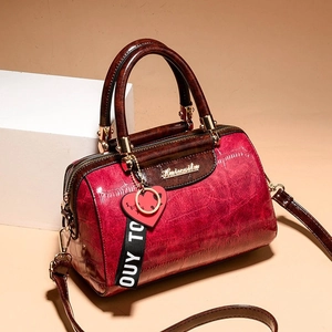 Red crocodile pattern Boston handbag with heart charm and wide strap on white stand