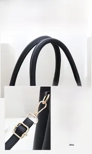 Details langer Ledergriffe und glänzender goldener Metallbeschläge an schwarzer Handtasche