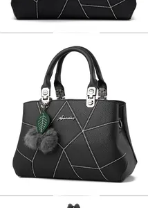 Detail of black pebbled leather handbag featuring white geometric stitching and pompom charm