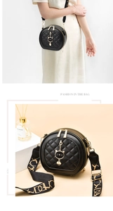 Detail of black quilted cylindrical crossbody bag with gold cat charm and wide strap