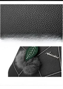 Detail of black pebbled leather handbag with contrast stitching and decorative pompom charm