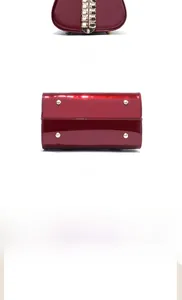 Detail view of burgundy patent leather bag base with golden protective rivets and chain