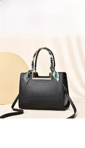 Detail of black crocodile texture handbag with silk scarf and gold metal handle