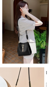 Detail of black leather bucket bag featuring golden cat charm and striped strap