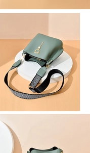 Detail of green bucket bag featuring a golden cat ornament and tassel with wide strap