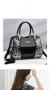 Detail of black patent leather handbag with golden sequin floral embroidery and metallic logo