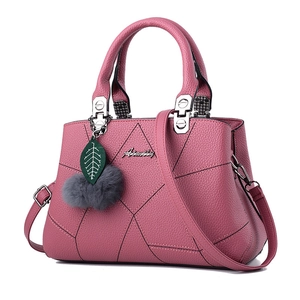 Pink quilted crossbody handbag with litchi texture and fur pompom charm on white background