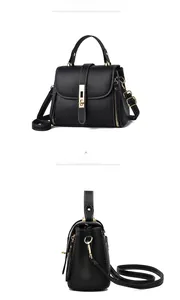 Detail of black litchi leather handbag with gold metal lock and side zipper accents