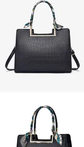 Detail of black crocodile embossed handbag with decorative silk scarf and gold handle