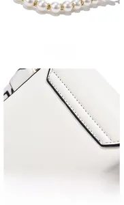 Detail of white leather shoulder bag with decorative pearl pendant and smooth fabric texture