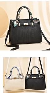 Detail of crocodile-textured faux leather bag with gold buckle and silk scarf handle decor