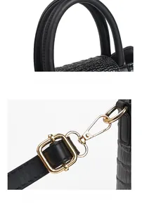 Detail of crocodile embossed leather handle with polished gold metal hardware on black bag