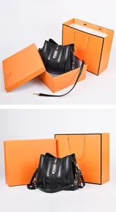 Detail view of black bucket bag with wave texture, gold clasp, and orange gift packaging