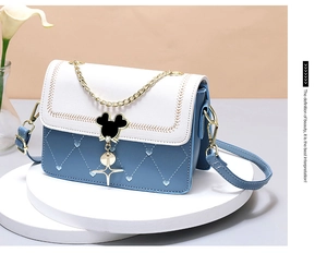 Detail of blue heart-quilted crossbody bag with white flap and metal cartoon mascot clasp