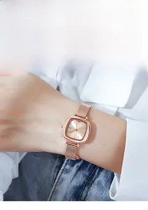 Detail of rose gold square watch with mesh band worn with casual shirt and jeans