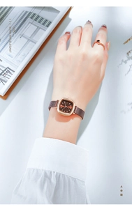 Close-up of rose gold square quartz watch with a brown dial and mesh metal strap on wrist