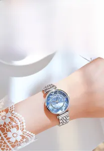 Close-up of silver mesh strap watch with blue sunray dial and crystal bezel on wrist