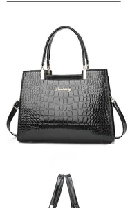 Detail of black crocodile pattern patent leather handbag with gold metal logo and sturdy handles