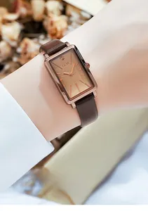 Montre rectangulaire élégante avec boîtier or rose et bracelet cuir marron au poignet