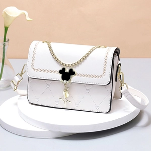White heart-quilted leather crossbody bag with iconic mouse clasp on white podium