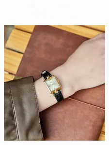 Primo piano dell'elegante orologio rettangolare dorato con cinturino in pelle nera