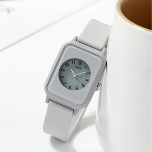 Minimalist grey rectangular quartz watch with silicone strap leaning on a white ceramic mug