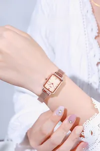 Detail of rose gold square watch with Milanese mesh strap worn on a wrist